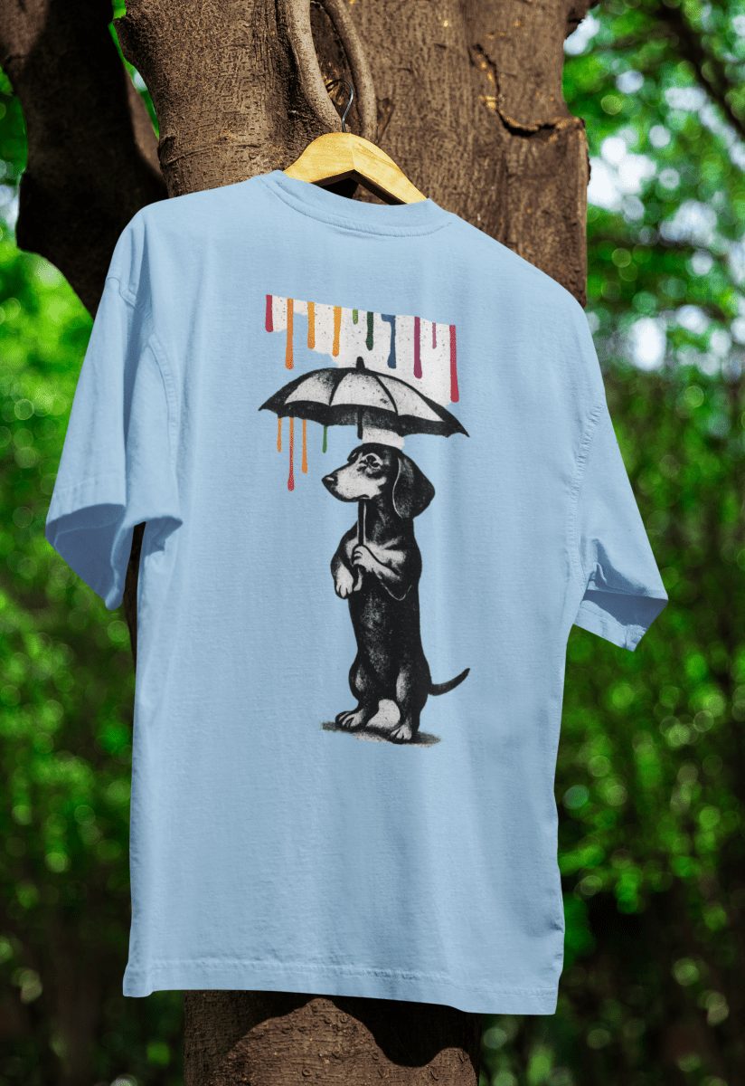 Hellblaues T-Shirt mit Dackel-Motiv unter Regenschirm und buntem Farbregen im Banksy-inspirierten Street-Art-Stil für Kunstliebhaber.