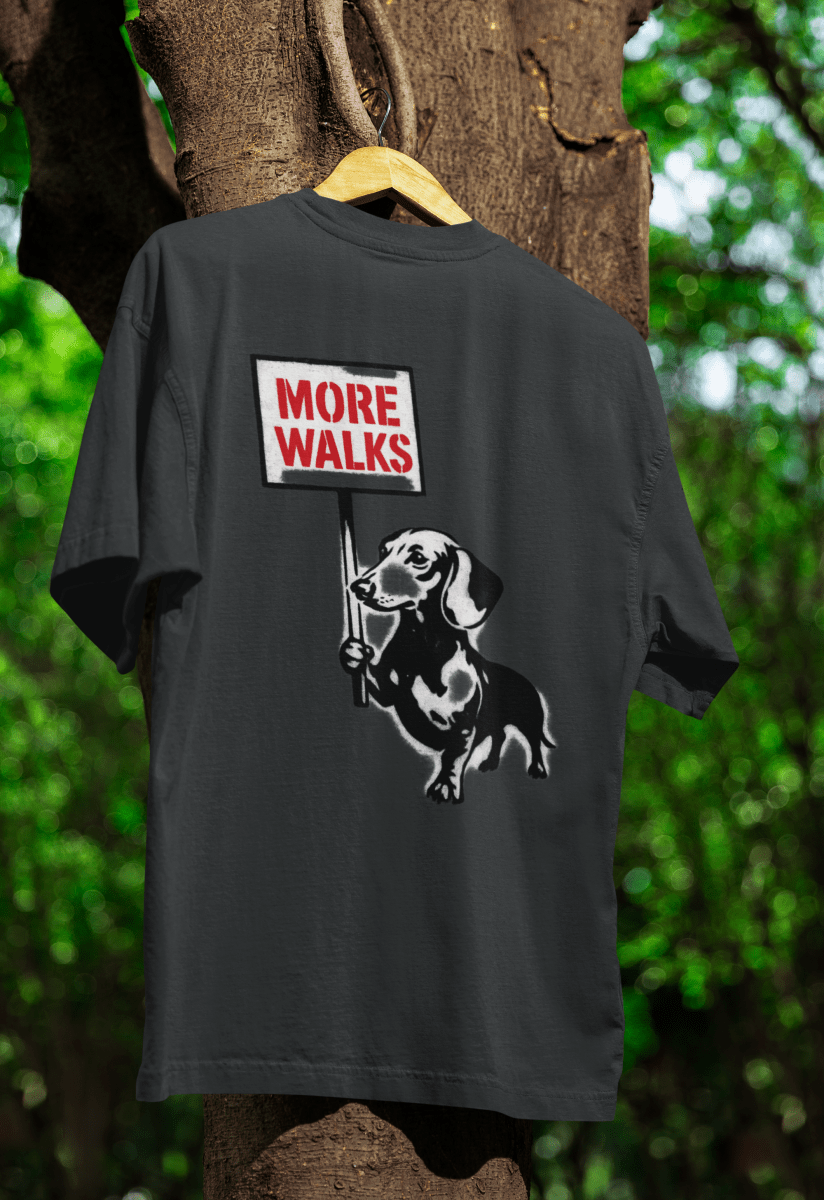 Schwarzes T-Shirt mit Schriftzug More-Walks und Dackel mit Protestschild im Banksy-inspirierten Street-Art-Stil fuer Hundeliebhaber.