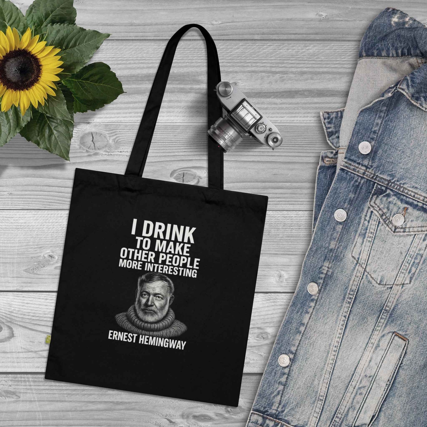 Zeigt eine schwarze Bio-Baumwoll-Tote-Bag in Frontansicht mit Ernest-Hemingway-Porträt und Zitat in weißer Druckgrafik, von True Insights.