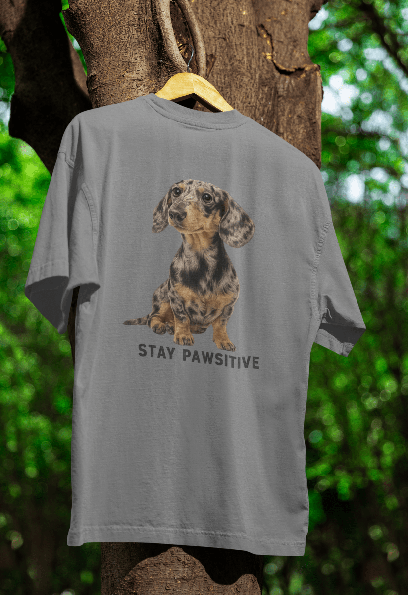 Graues T-Shirt mit Dackel-Motiv und Schriftzug Stay-Pawsitive im realistischen Tier-Porträt-Stil für Hundeliebhaber.